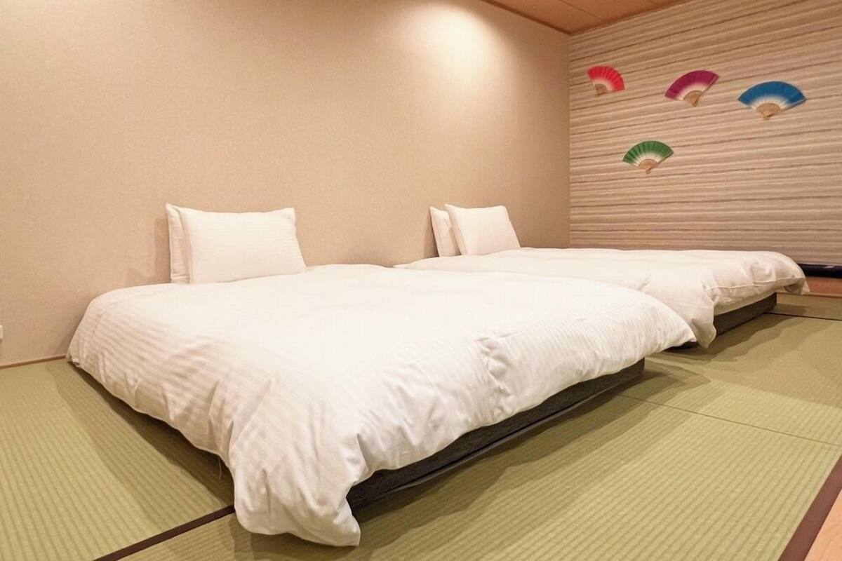 A room with two beds, a tatami mat floor, and a wall with decorative fans.