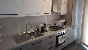 A modern kitchen with white cabinets, a stainless steel sink, a gas stove, and a microwave. - Airport bari deluxe  (Bari)