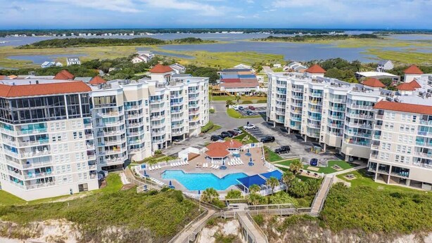 A high-rise hotel with multiple balconies, a central pool, and a view of the surrounding landscape. - Oceanfront Resort Retreat Stunning Ocean Views (North Topsail Beach)