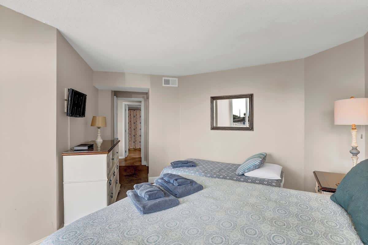 A bedroom with two beds, a desk, a mirror, and a lamp.