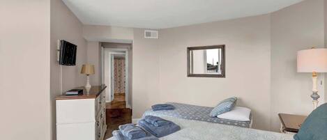 A bedroom with two beds, a desk, a mirror, and a lamp.