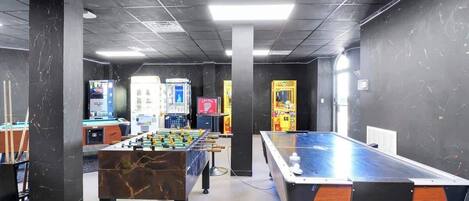 Una habitación con mesa de fútbol, mesa de billar y varios juegos de arcade.