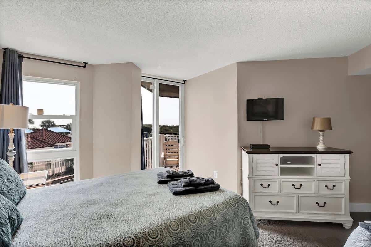 A bedroom with a bed, a dresser, a TV, and a balcony with a view.
