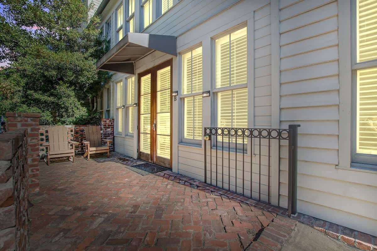 A two-story house with a brick patio, wooden chairs, and a metal gate.