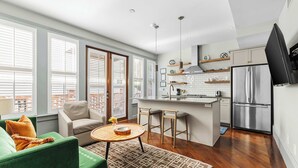A modern kitchen with a stainless steel refrigerator, white tiled backsplash, and wooden bar stools. - The Harmony | Historic 2BR, Steps to King Street (Charleston)
