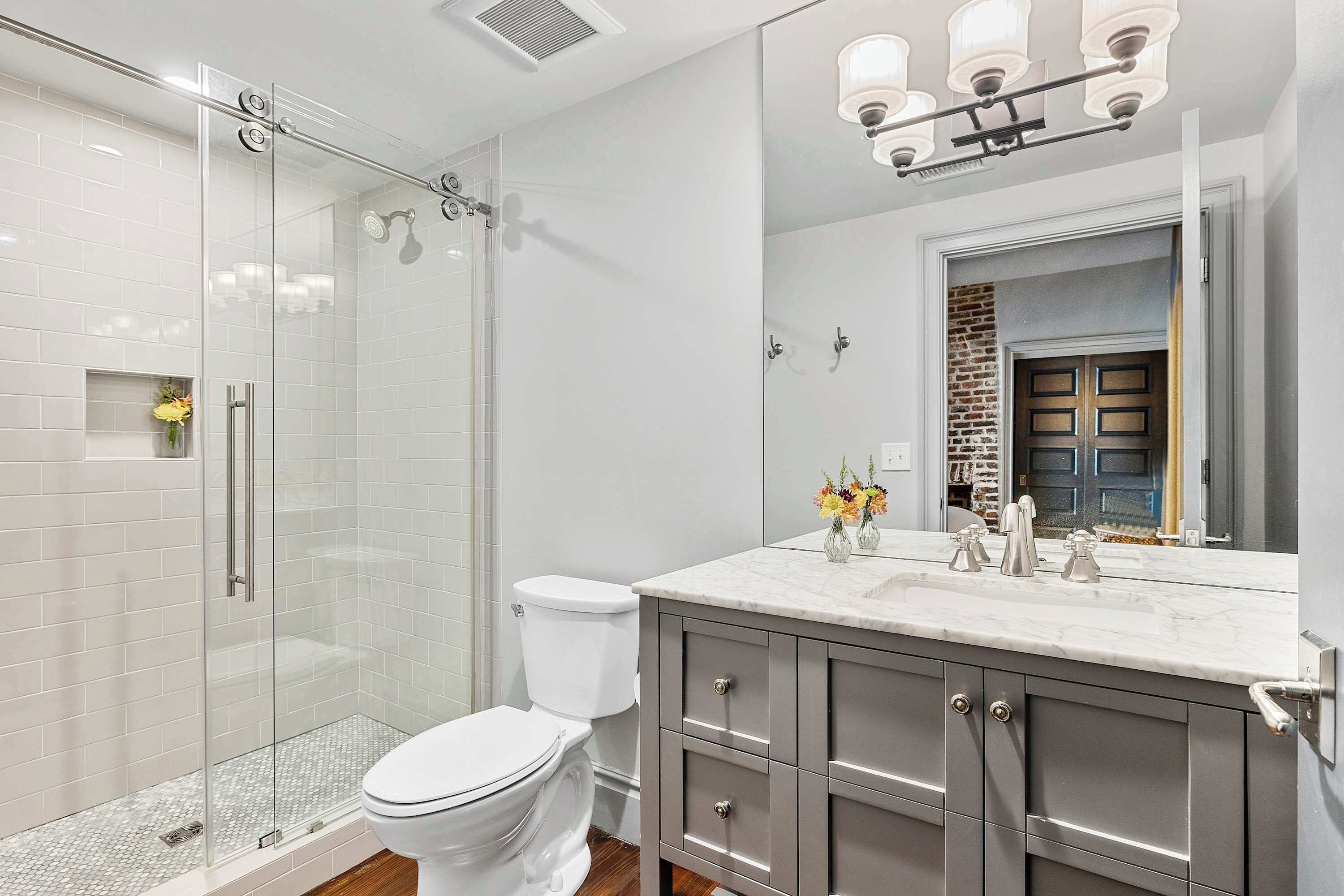 Uma casa de banho moderna com chuveiro em cabine de vidro, sanita branca e lavatório de mármore com espelho em cima.