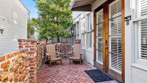 A brick patio with two wooden chairs, a door with a 'B' sign, and a brick wall. - The Harmony | Historic 2BR, Steps to King Street (Charleston)