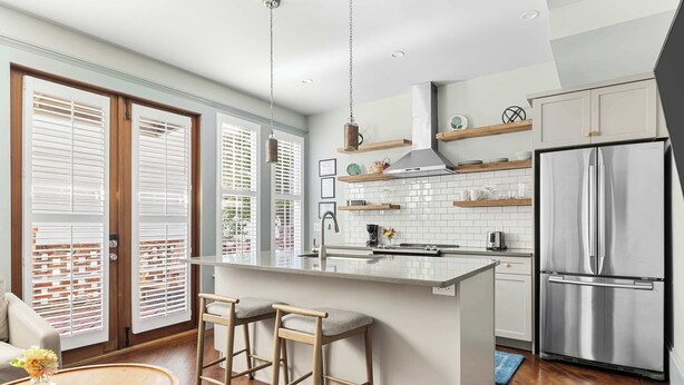 A modern kitchen with a central island, stainless steel appliances, and wooden bar stools. - The Harmony | Historic 2BR, Steps to King Street (Charleston)