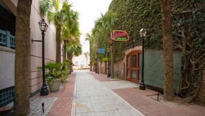 A narrow alleyway with a brick pathway, palm trees, and a building with a neon sign. - The Rhythm | Charming 1BR in Prime Location! (Charleston)