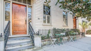 A two-story house with a wooden front door, a number '15' on the wall, and a small outdoor seating area with chairs and tables. - The Rhythm | Charming 1BR in Prime Location! (Charleston)
