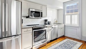 A modern kitchen with stainless steel appliances, white cabinetry, and a patterned rug. - The Rhythm | Charming 1BR in Prime Location! (Charleston)