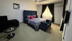 Un dormitorio con una cama, un sofá negro, una mesita redonda y un televisor.