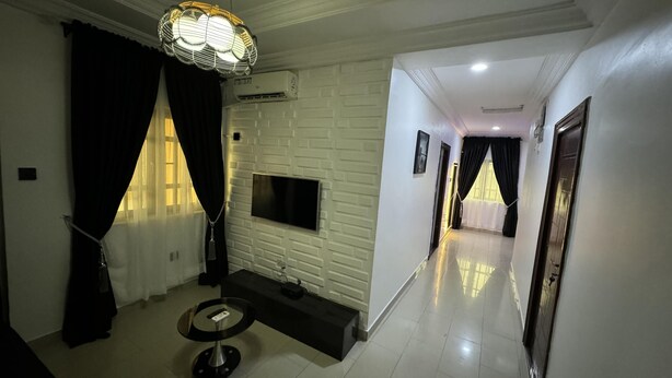 Una sala de estar moderna con un televisor de pantalla plana montado en una pared con diseño de ladrillo blanco, una mesa redonda y una lámpara colgante.