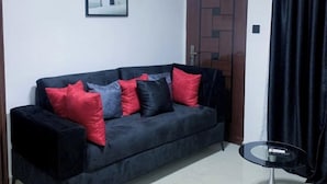Un sofá de color oscuro con varios cojines en rojo, gris y negro, ubicado frente a una pared blanca con un cuadro enmarcado encima.