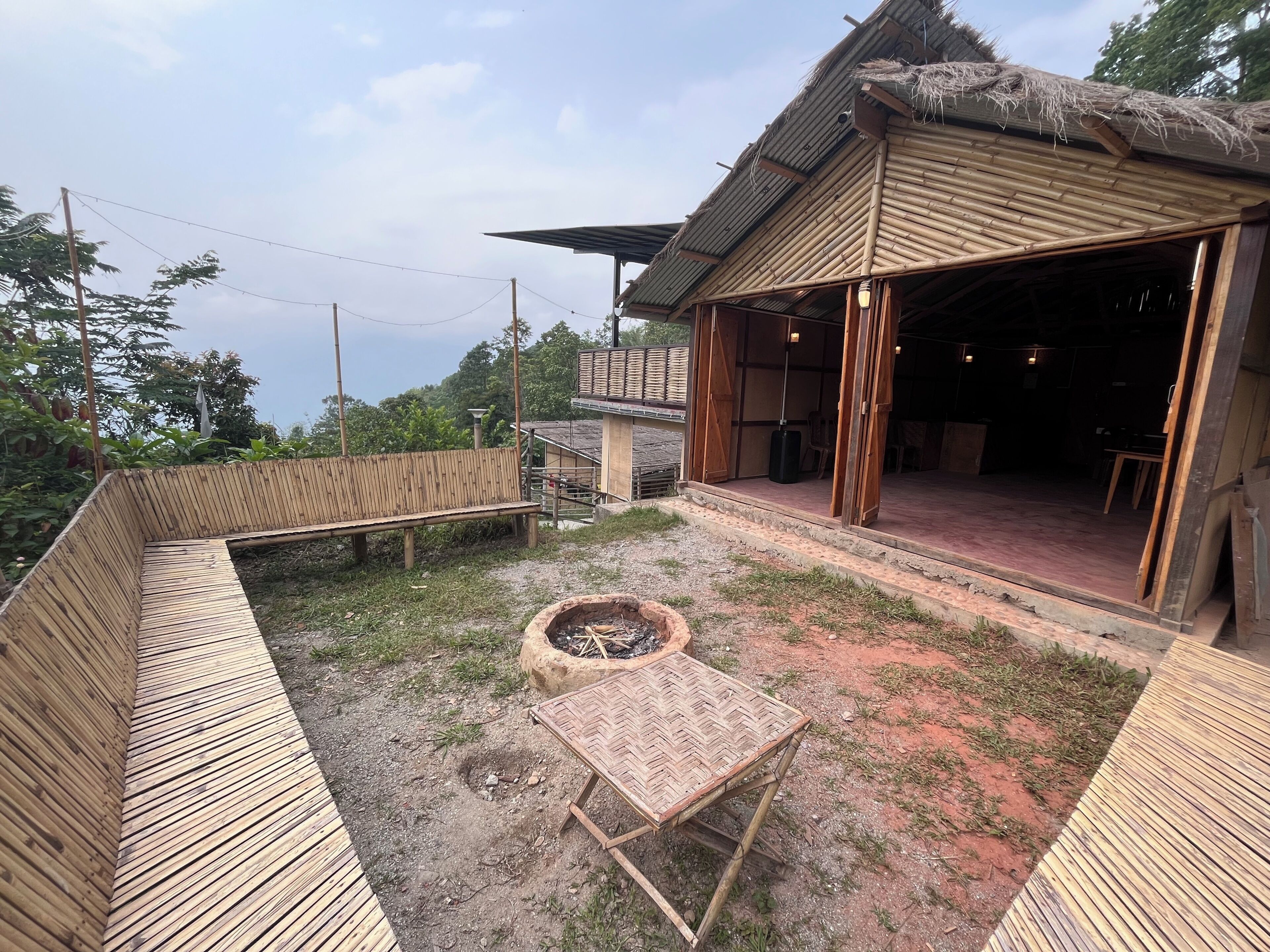 Une structure en bambou avec un toit de chaume, un foyer et un banc en bois.