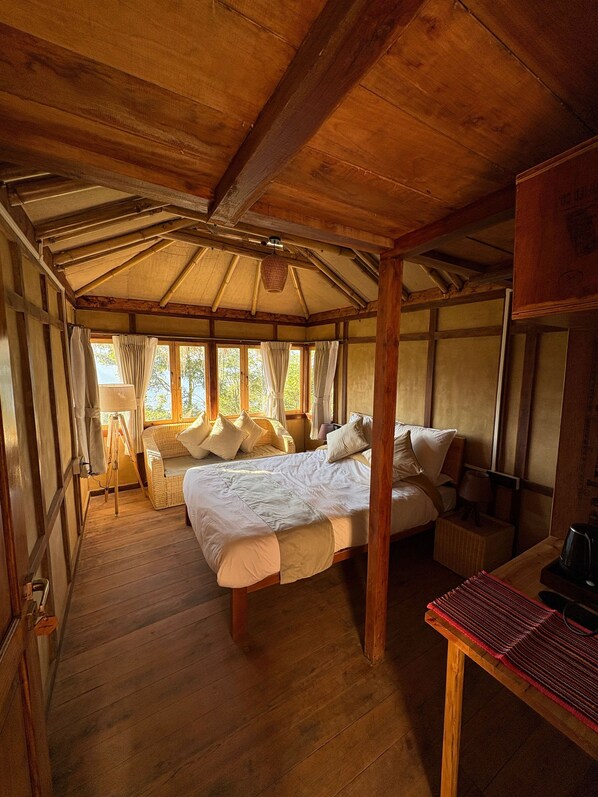 A wooden cabin bedroom with a bed, a small table, and a wicker chair. - Art Mile Kalimpong (Kalimpong)