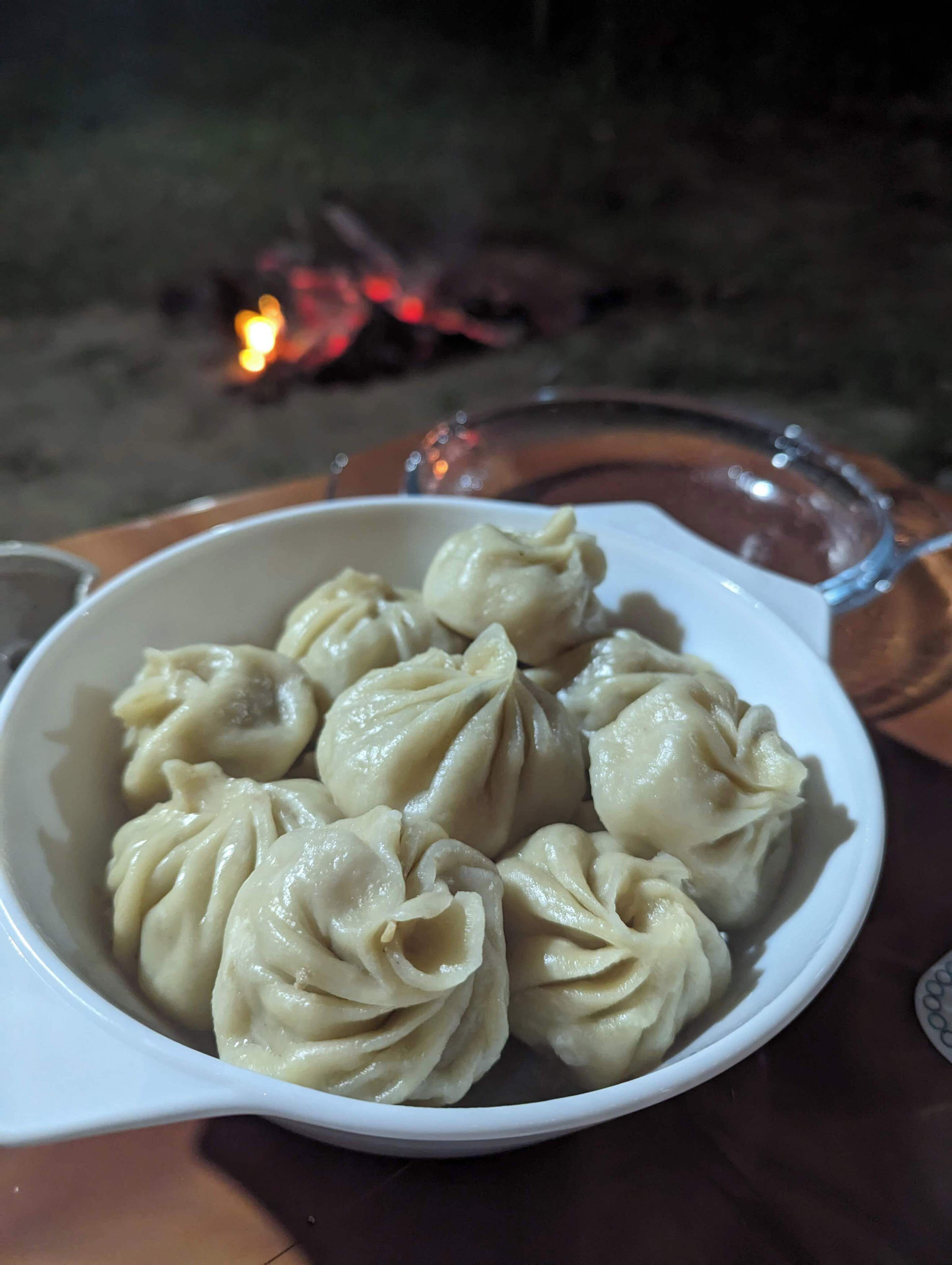 A bowl of dumplings on a table with a glass and a candle in the background.