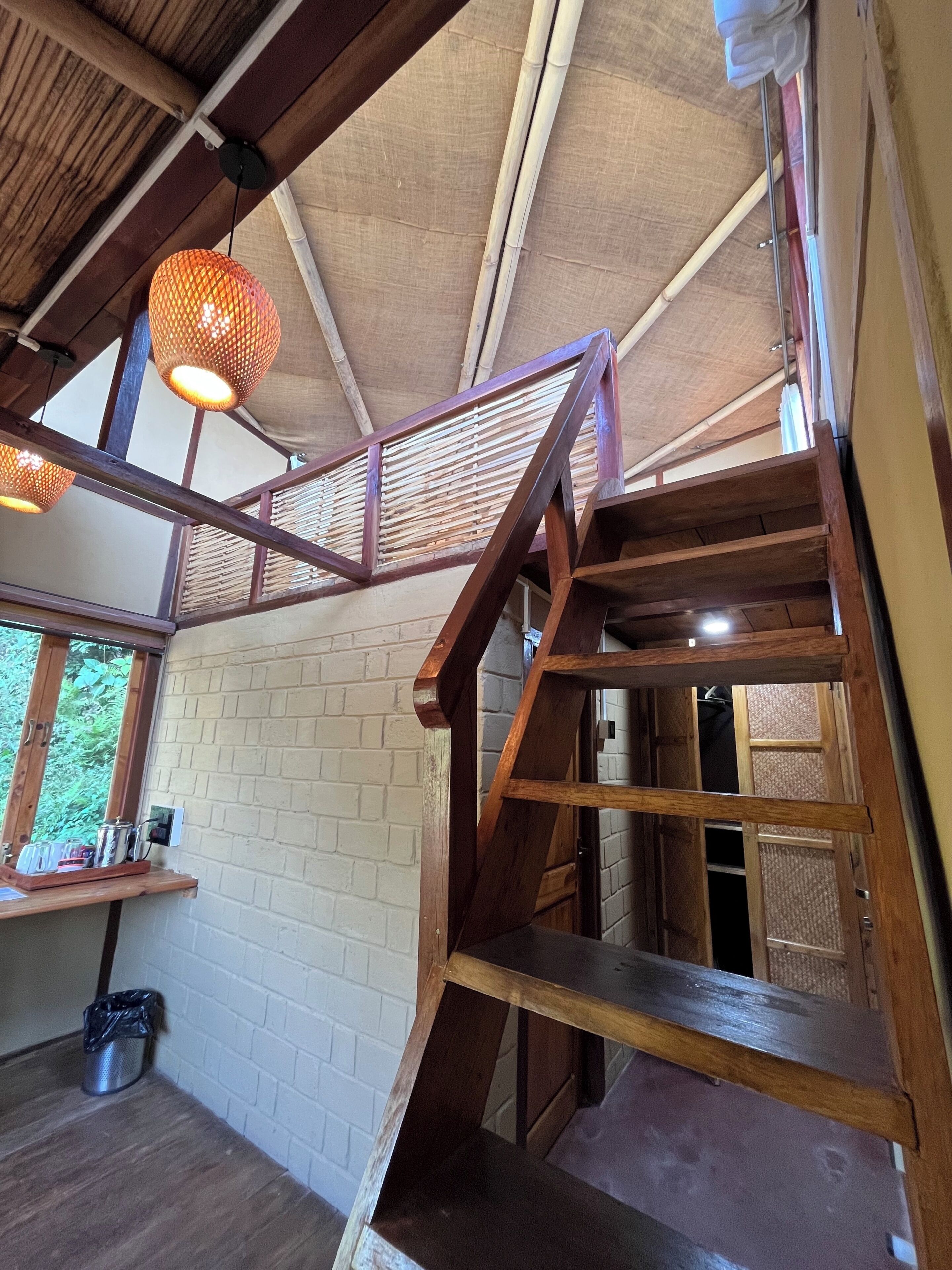 Una escalera de madera con barandilla de metal, un muro de ladrillo y una ventana con vista a zonas verdes.