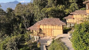 A resort with thatched-roof buildings, a concrete pathway, and lush greenery. - Art Mile Kalimpong (Kalimpong)