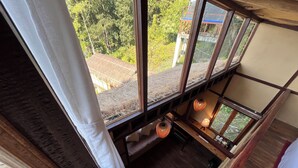 A room with a view of a thatched roof structure outside, wooden beams, and a hanging light fixture. - Art Mile Kalimpong (Kalimpong)