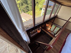 A room with a view of a thatched roof structure outside, wooden beams, and a hanging light fixture. - Art Mile Kalimpong (Kalimpong)