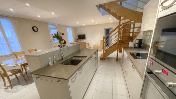 Una cocina moderna con una isla central, una escalera de madera y un horno empotrado.