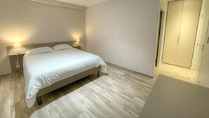 Un dormitorio con cama, lámparas de noche, armario y suelo de madera.