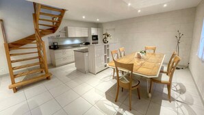 Una cocina moderna con armarios blancos, una escalera de madera y un comedor con una mesa y sillas de madera.