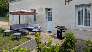 Un edificio de fachada de piedra, con un amplio patio que incluye un sofá gris, una mesa y una sombrilla.