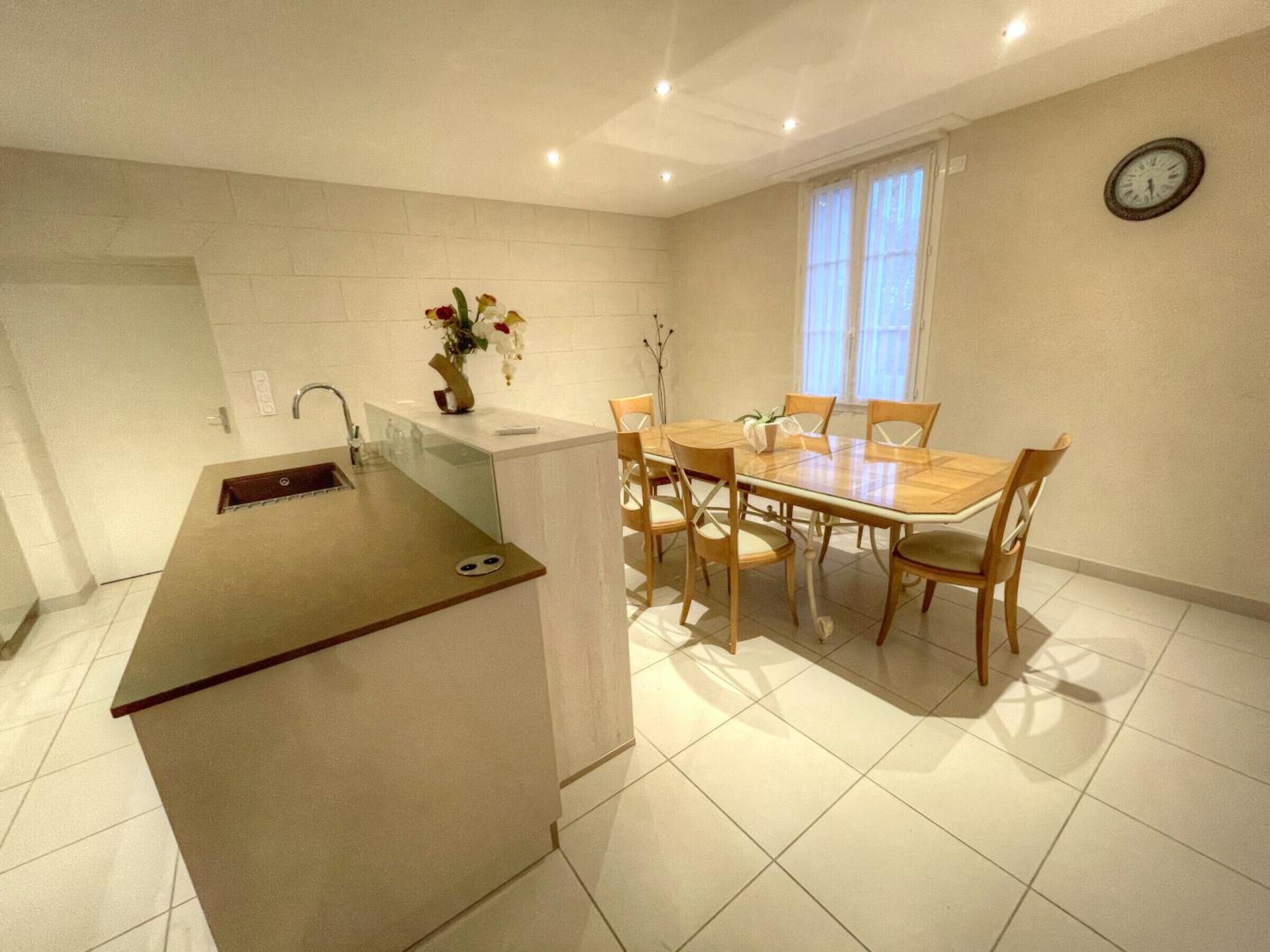 Una cocina compacta con comedor, que incluye una mesa y sillas de madera, una pequeña isla con pileta y un reloj en la pared.