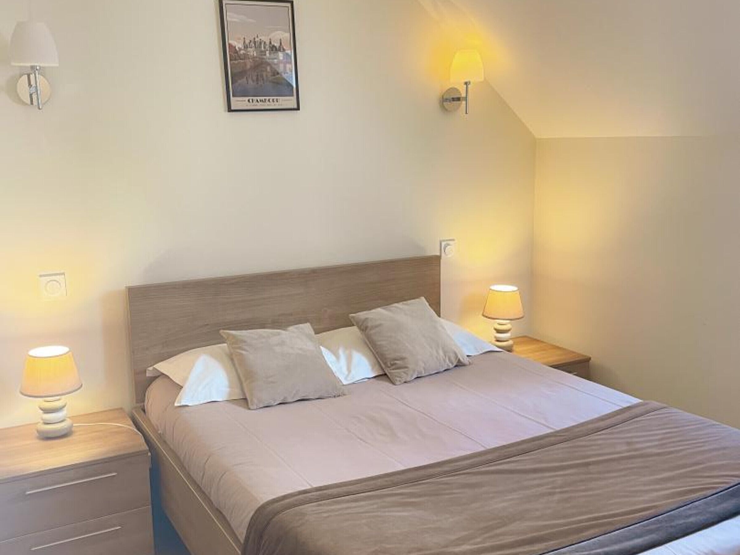 Ein ordentlich bezogenes Bett mit zwei Kissen, einem hölzernen Kopfteil und Nachttischlampen an beiden Seiten.