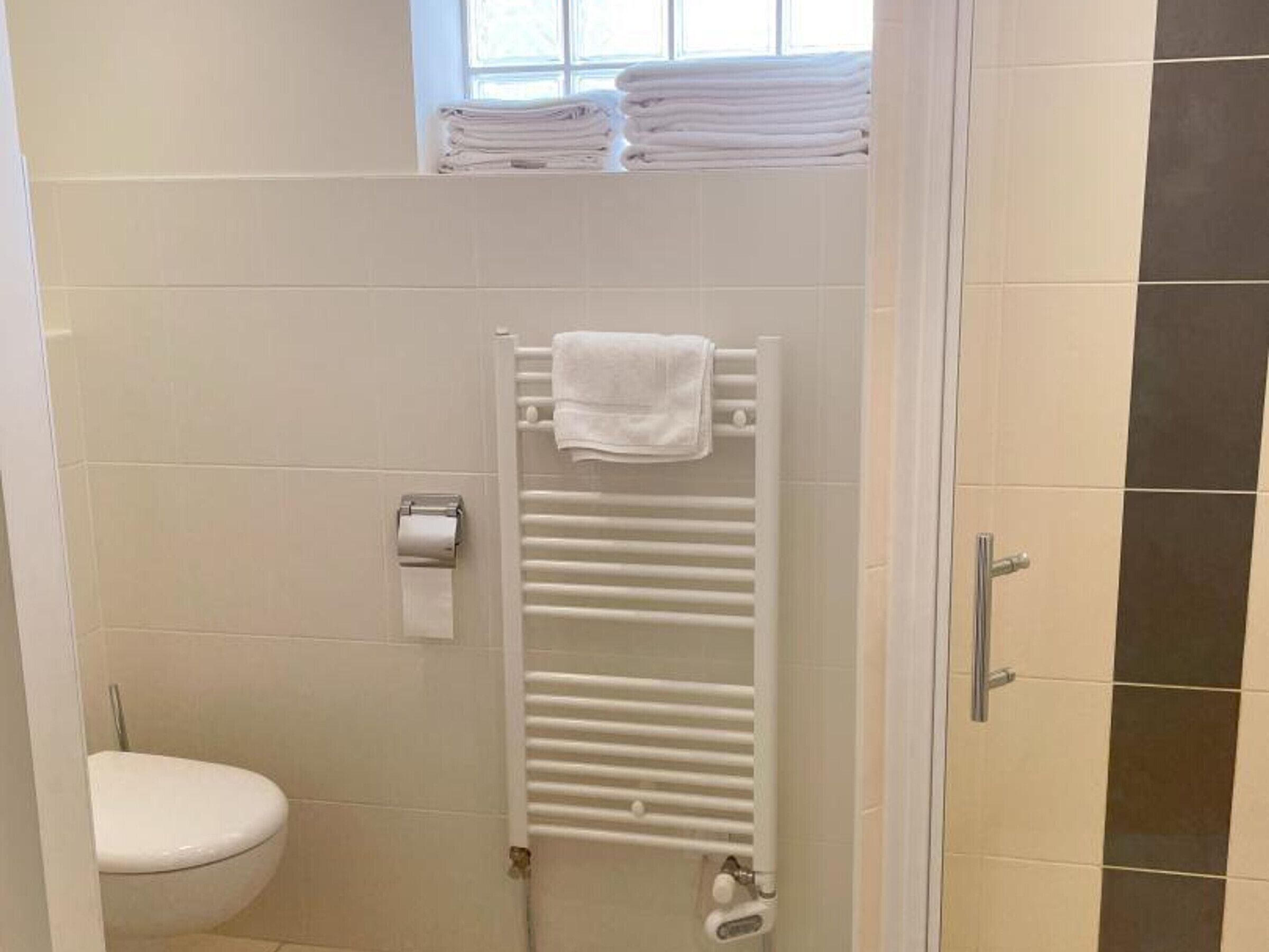 A bathroom with a white toilet, a towel rack with folded towels, and a paper towel dispenser.