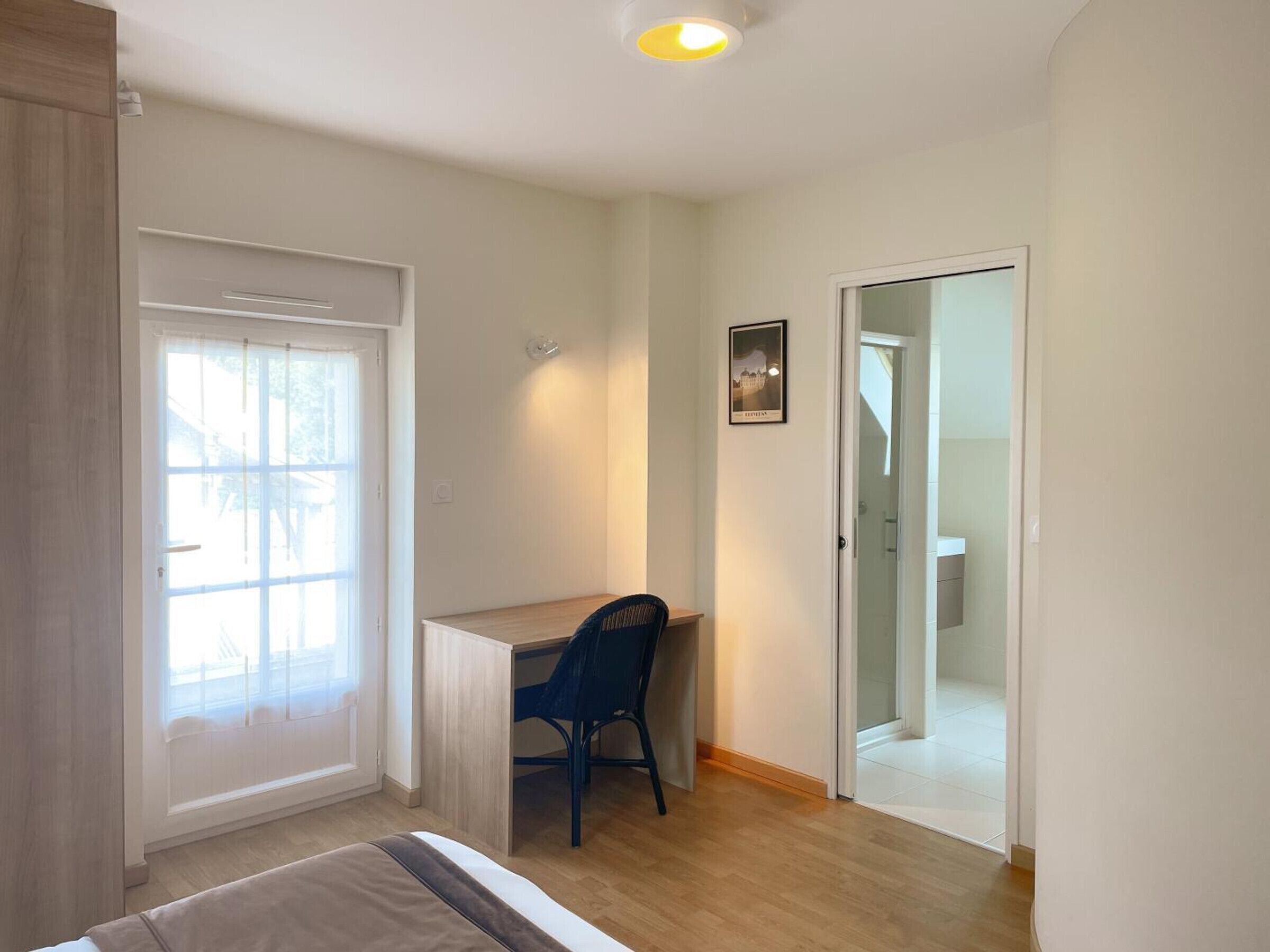 Une chambre à coucher comprenant un lit, un bureau, une chaise, une fenêtre et une porte donnant sur une salle de bain.