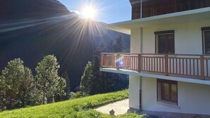 En toetagers bygning med balkon, omgivet af grønt og bjerge.