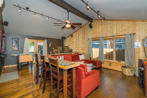 A cozy living room with a wooden ceiling, a red sofa, a wooden table, and a foosball table.