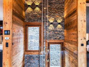 A narrow hallway with wooden walls and a stone accent wall. There are two doors with glass panels and a small window.