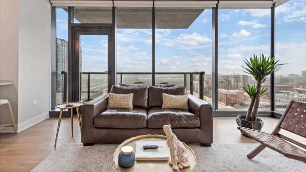 A modern living room with a brown leather sofa, a small side table, a coffee table, and a potted plant.