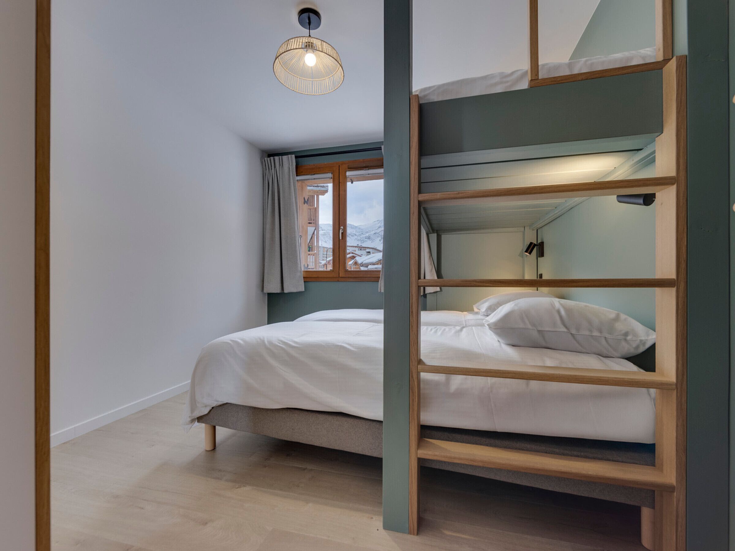 Een slaapkamer met een stapelbed, raam, houten vloer en een hanglamp.