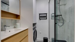 Et moderne badeværelse med en glasbrusekabine, en indbygget vask og et trækommode.