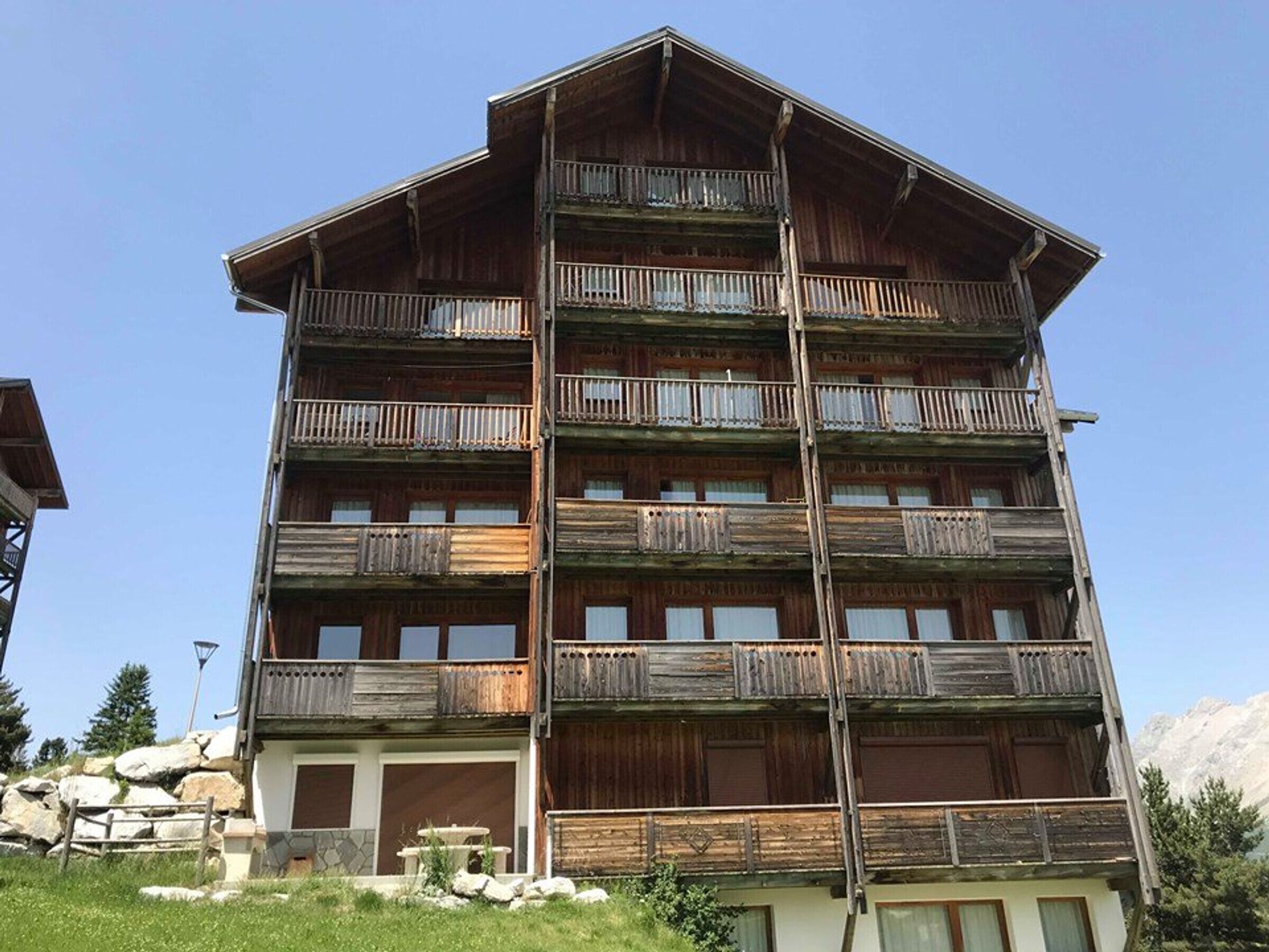 Un edificio de madera de varios pisos con balcones, un muro de piedra y cielo despejado.