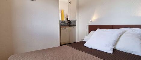 Une chambre d’hôtel avec un lit, une petite kitchenette et une salle de bain visible à travers une porte ouverte.