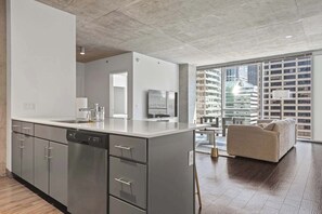 A modern kitchen with a dishwasher, a large island, and a sofa in a spacious living area with a city view.