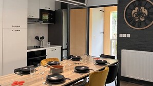 A modern kitchen with a dining area, featuring a large wooden table, black and yellow chairs, and a wall-mounted clock. - Duplex lodge for 8 people, 3 parking spaces, near center (Cauterets)