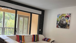 A modern living room with a white sofa, colorful striped pillows, a wooden coffee table, and a large window with blinds. - Duplex lodge for 8 people, 3 parking spaces, near center (Cauterets)