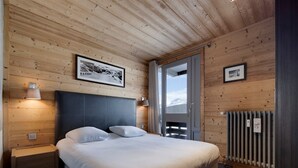 A bedroom with a wooden ceiling, a bed with white linens, two bedside lamps, and a framed picture on the wall. - Bright apartment, ski-in/ski-out, WIFI (Tignes)