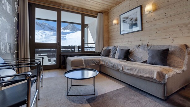 A cozy room with a wooden ceiling, a sofa, a coffee table, and a large window offering a mountain view. - Bright apartment, ski-in/ski-out, WIFI (Tignes)