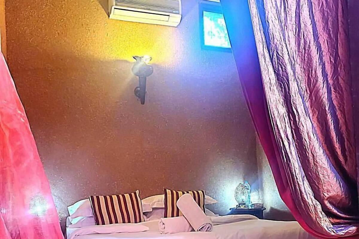 A bed with striped pillows, a nightstand with a lamp, and a wall-mounted air conditioner.
