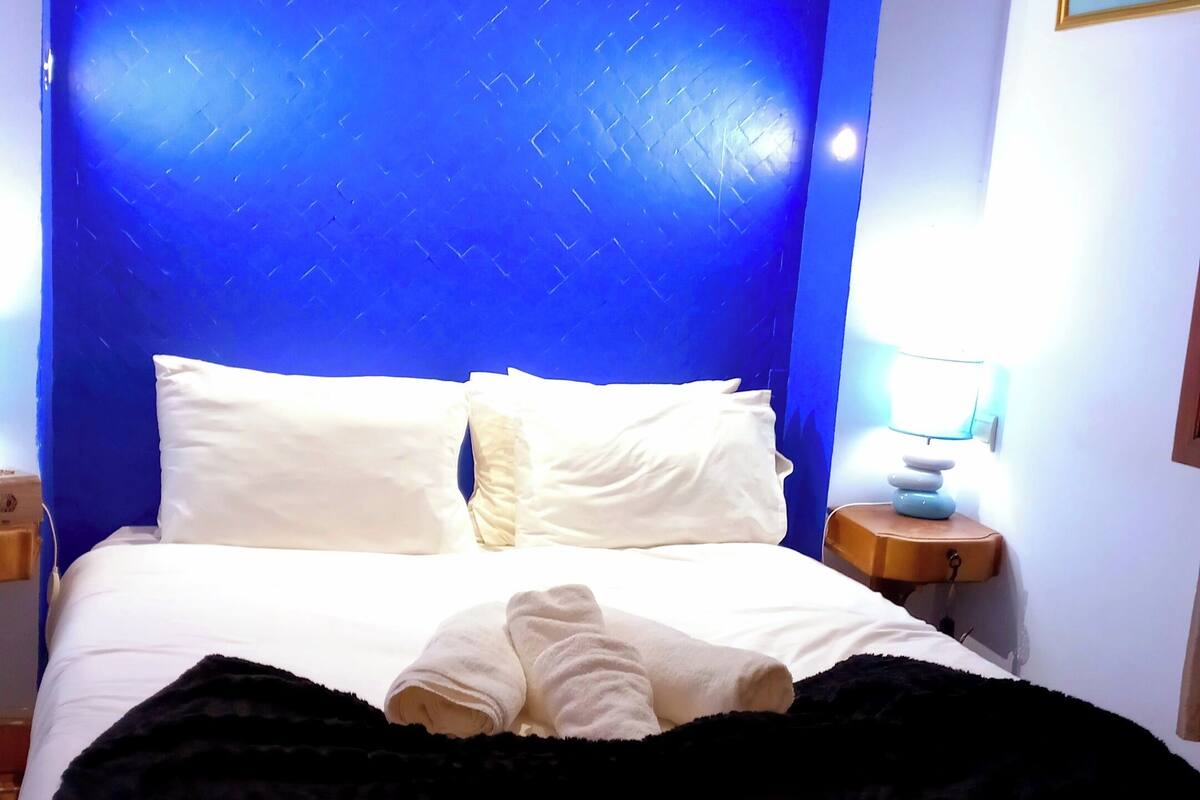 A hotel room with a large bed, a bedside table with a lamp, and a framed picture on the wall.