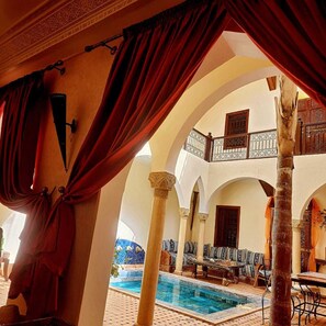 Area piscina interna con zona relax, colonne e balcone con ringhiere decorate.