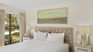 A hotel room with a large bed, two bedside tables with lamps, a painting above the bed, and a view of the outdoors through a window. - 1BR Lakefront Condo Sandestin w/ Golf Cart (Miramar Beach)